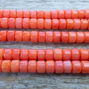 Puede incluir: Una hebra de cuentas de coral, de color naranja brillante, dispuestas en tres filas sobre una superficie de madera.