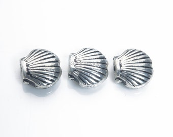 May include: Three silver-colored metal beads shaped like seashells. The beads have a detailed, textured surface.