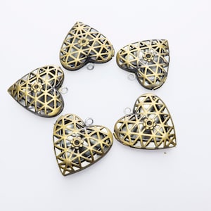 Puede incluir: Cinco colgantes en forma de corazón de color bronce con intrincados calados geométricos y pequeños detalles florales. Cada colgante tiene un pequeño lazo para sujetarlo a una cadena. Los colgantes están dispuestos en forma de estrella sobre un fondo blanco.