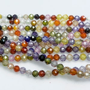 May include: A strand of faceted gemstone beads in various colors, including green, purple, orange, and yellow. The beads are round and have a faceted finish.
