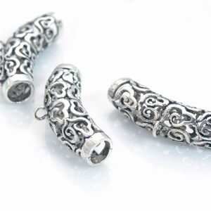 Pode incluir: Tr&ecirc;s tampas de extremidade decorativas de metal prateado para a fabrica&ccedil;&atilde;o de joias. Cada tampa tem um design intrincado e ornamentado com uma forma curva.