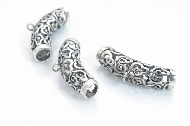 Pode incluir: Tr&ecirc;s tampas de extremidade decorativas de metal prateado para a fabrica&ccedil;&atilde;o de joias. Cada tampa tem um design intrincado e ornamentado com uma forma curva.