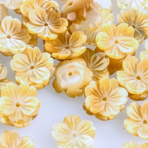 Könnte beinhalten: Eine Sammlung von gelben, irisierenden Perlmutt-Blumenperlen. Die Perlen haben ein geschnitztes Design und ein Loch in der Mitte zum Aufziehen.