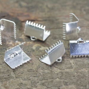 May include: Six silver metal clasps with a serrated edge and a small loop on each. The clasps are arranged on a brown wooden surface.