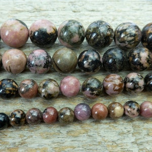 Puede incluir: Cadenas de cuentas de piedras preciosas pulidas de varios tama&ntilde;os. Las cuentas muestran una mezcla de tonos rosa, negro y marr&oacute;n, con un aspecto veteado. Ideal para la fabricaci&oacute;n de joyas.