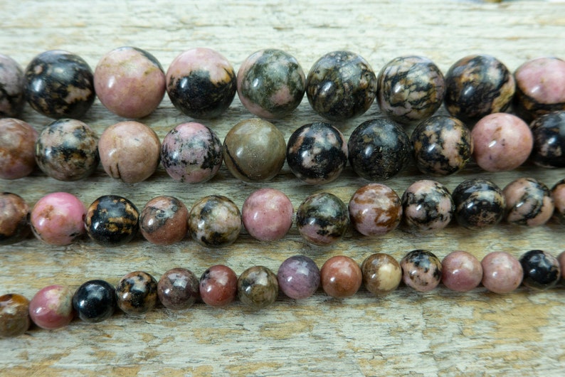 Puede incluir: Cadenas de cuentas de piedras preciosas pulidas de varios tama&ntilde;os. Las cuentas muestran una mezcla de tonos rosa, negro y marr&oacute;n, con un aspecto veteado. Ideal para la fabricaci&oacute;n de joyas.