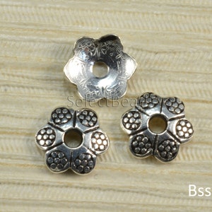 May include: Three silver flower-shaped bead caps with a small hole in the center. The bead caps have a textured design.
