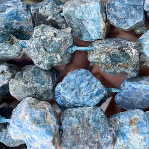 Könnte beinhalten: Eine Kette aus blauen Kyanit-Perlen, jede Perle hat eine raue, natürliche und unregelmäßige Form. Die Perlen sind mit einer hellblauen Schnur aneinandergereiht.