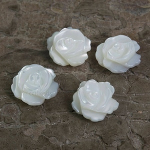 Może przedstawiać: Cztery białe perłowe ozdoby w kształcie róży. Róże są rzeźbione z białej muszli i mają delikatny, realistyczny wygląd.