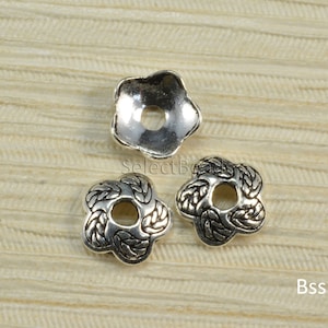 May include: Three silver metal flower-shaped bead caps with a decorative design. The bead caps have a hole in the center for stringing.