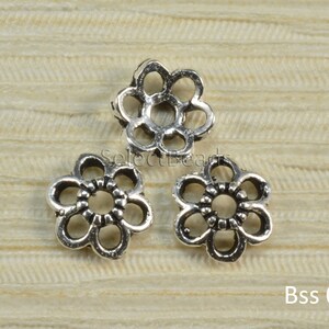 May include: Three silver metal flower-shaped bead spacers. The spacers have a delicate, openwork design.