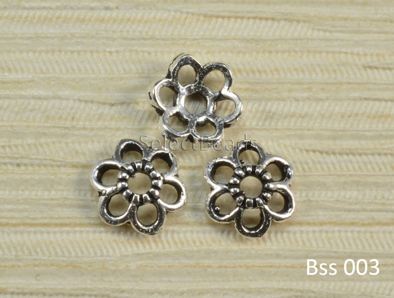 May include: Three silver metal flower-shaped bead spacers. The spacers have a delicate, openwork design.