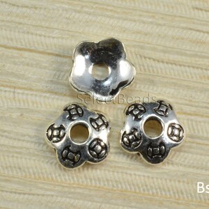 May include: Three silver flower-shaped bead caps with a small hole in the center. The bead caps have a raised design on the surface.