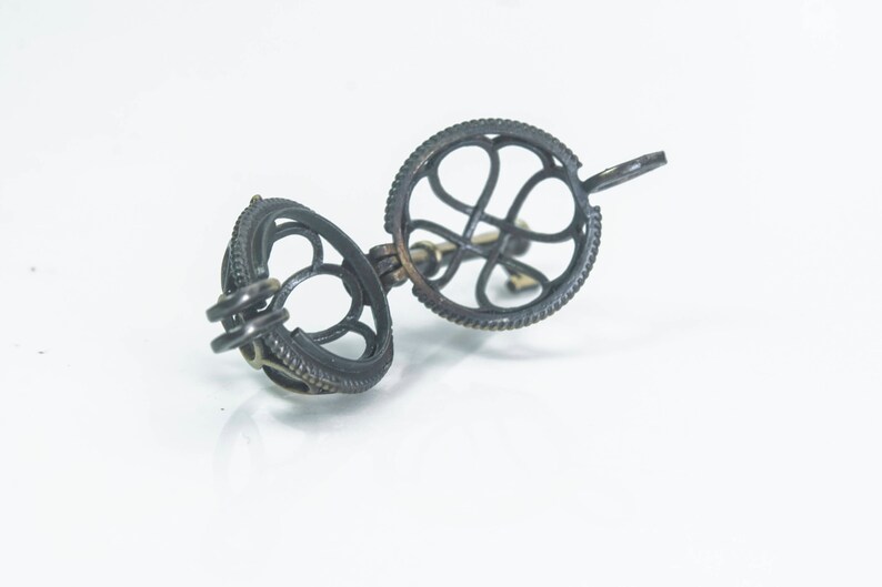 May include: A silver-toned metal cage pendant with a delicate openwork design. The cage is open on one side and has a small loop at the top for attaching to a chain.