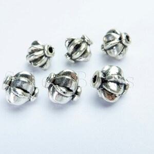 May include: Six silver metal beads with a decorative design. The beads are round and have a textured surface.