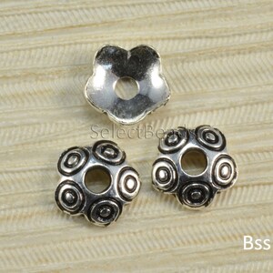 May include: Three silver metal flower-shaped bead caps with a hole in the center. The bead caps have a swirl design.