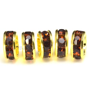 May include: Four gold-toned bead spacers with a row of brown rhinestones around the circumference.