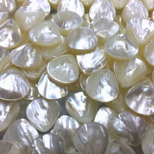 May include: A close-up of a pile of white, iridescent, shell-shaped beads. The beads have a smooth, polished finish and a slightly irregular shape.