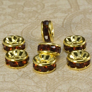 May include: Eight gold-toned bead caps with a row of dark brown rhinestones around the edge. The bead caps are designed to be used as a spacer or connector for jewelry making.