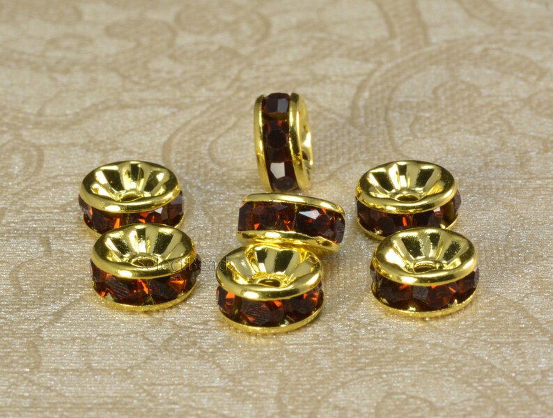 May include: Eight gold-toned bead caps with a row of dark brown rhinestones around the edge. The bead caps are designed to be used as a spacer or connector for jewelry making.