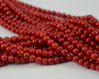 May include: A strand of bright red coral beads. The beads are round and smooth, and they are all about the same size. The beads are strung on a clear thread.