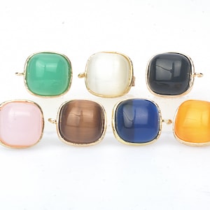 May include: Eight square-shaped gemstone charms with gold-toned metal settings. The charms are in various colors, including green, white, black, pink, brown, blue, and orange.