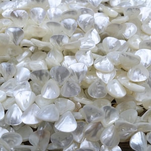 May include: A close-up of a pile of white, pearlescent, triangular-shaped beads. The beads are smooth and shiny, and they have a slightly iridescent sheen.