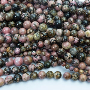 Puede incluir: Una colecci&oacute;n de cuentas redondas de piedras preciosas en varios tama&ntilde;os y tonos de rosa, marr&oacute;n y negro. Las cuentas est&aacute;n ensartadas, creando una exhibici&oacute;n texturizada y colorida. Ideal para la fabricaci&oacute;n de joyas.