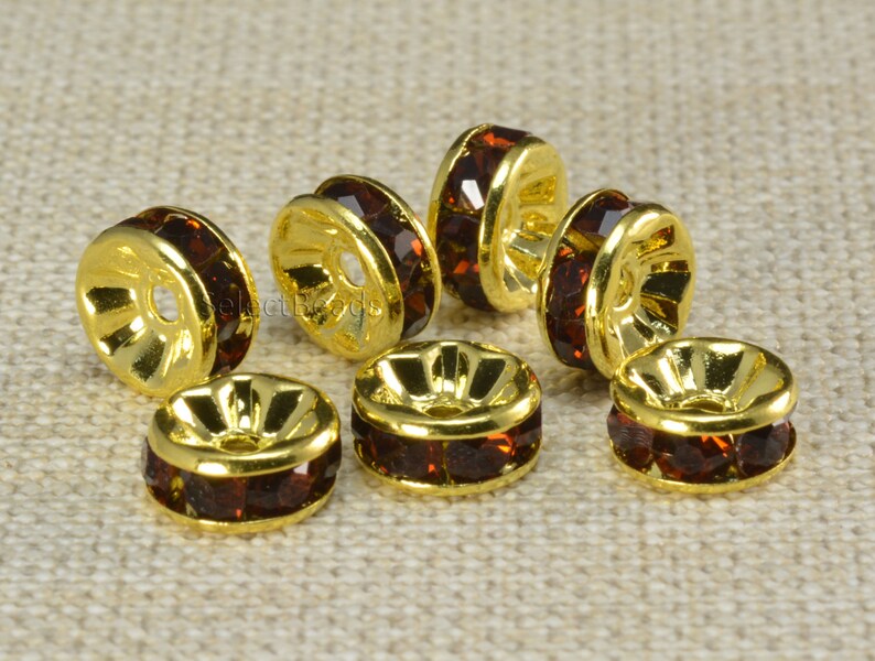 May include: Eight gold-toned metal bead caps with a single row of dark brown rhinestones around the edge.