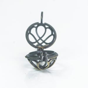 May include: A silver metal locket with a heart-shaped design. The locket is open and the inside is visible. The locket has a loop at the top for attaching a chain.