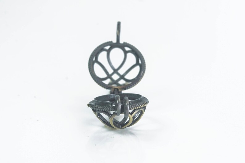 May include: A silver metal locket with a heart-shaped design. The locket is open and the inside is visible. The locket has a loop at the top for attaching a chain.