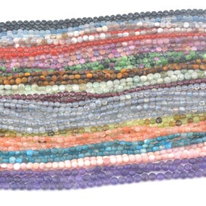May include: A collection of multiple strands of small, round, faceted gemstone beads arranged in horizontal rows. The strands display a wide spectrum of colors including black, red, green, brown, grey, orange, blue, pink, and purple hues.
