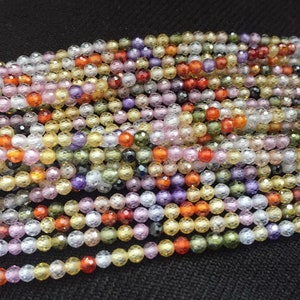 May include: A strand of faceted gemstone beads in various colors, including clear, yellow, orange, pink, purple, and green. The beads are small and round, with a textured surface.