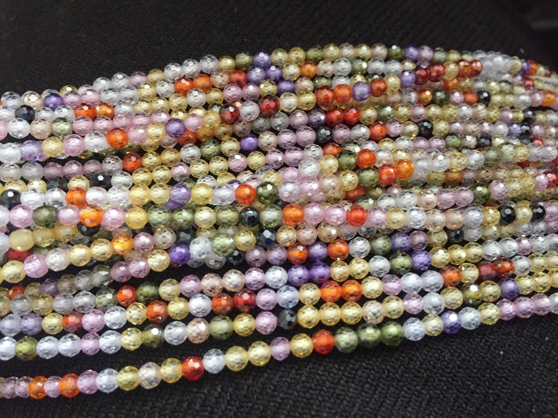 May include: A strand of faceted gemstone beads in various colors, including clear, yellow, orange, pink, purple, and green. The beads are small and round, with a textured surface.