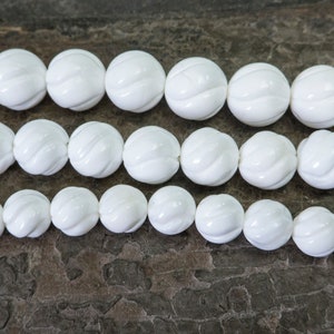 Puede incluir: Cuentas redondas blancas con un dise&ntilde;o tallado. Las cuentas est&aacute;n dispuestas en tres filas sobre una superficie de madera marr&oacute;n.