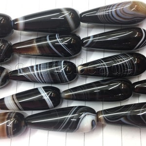 May include: A strand of black and white agate gemstone beads in a teardrop shape. The beads have a polished finish and are strung on a clear thread.