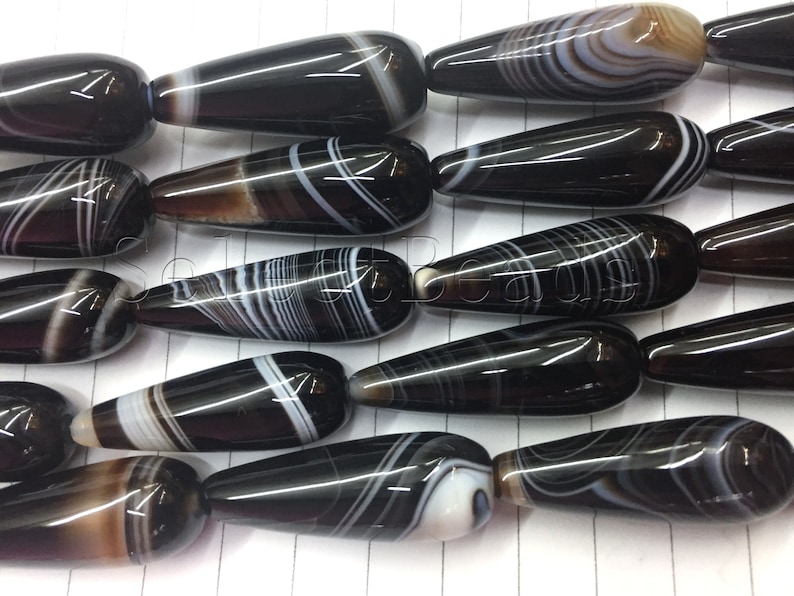 May include: A strand of black and white agate gemstone beads in a teardrop shape. The beads have a polished finish and are strung on a clear thread.