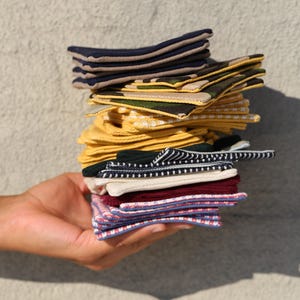 May include: A stack of folded socks in various patterns and colors, including navy, khaki, yellow, green, and burgundy. The socks are held in a hand against a neutral background.