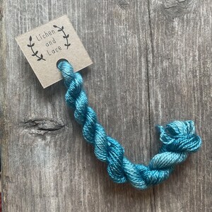 May include: A skein of teal blue embroidery floss with a brown tag that reads "Lichen and Lace".