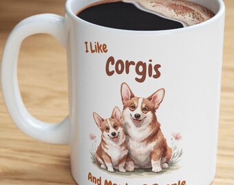Könnte beinhalten: Weiße Keramik-Kaffeetasse mit braunem Rand. Die Tasse zeigt ein Bild von zwei Corgis und den Text "Ich mag Corgis und vielleicht 3 Leute".