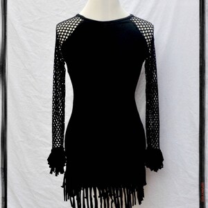 May include: Black long-sleeved dress with a mesh panel on the shoulders and a fringe hem.