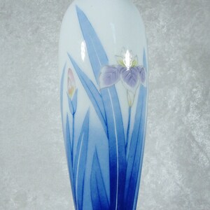 May include: A white ceramic vase with a blue and white floral design. The vase is decorated with a stylized iris flower and leaves.