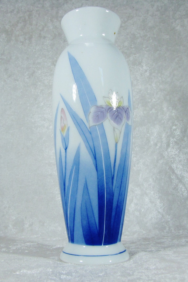 May include: A white ceramic vase with a blue and white floral design. The vase is decorated with a stylized iris flower and leaves.