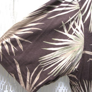 May include: Close-up of a brown short-sleeved shirt with a palm leaf pattern in shades of tan and green. The fabric is visible, showing the texture and the stitching of the sleeve.