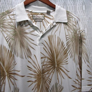 May include: White polo shirt with a tropical palm leaf pattern in shades of brown and green. The shirt has a light-colored collar and a button-down placket. The brand name "Pusser's Island Marine" is visible on a tag.