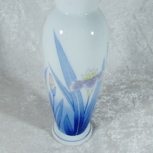 May include: A white ceramic vase with a blue and white floral design. The vase has a rounded body and a narrow neck. The floral design features blue leaves and pink and purple flowers.