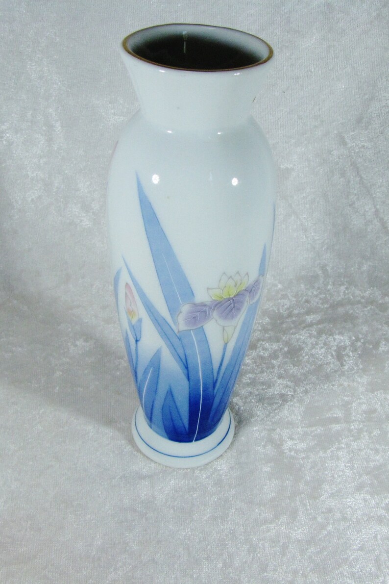 May include: A white ceramic vase with a blue and white floral design. The vase has a rounded body and a narrow neck. The floral design features blue leaves and pink and purple flowers.