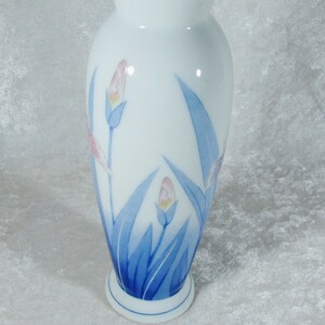 May include: A white ceramic vase with a blue and pink floral design. The vase has a rounded body and a flared top.