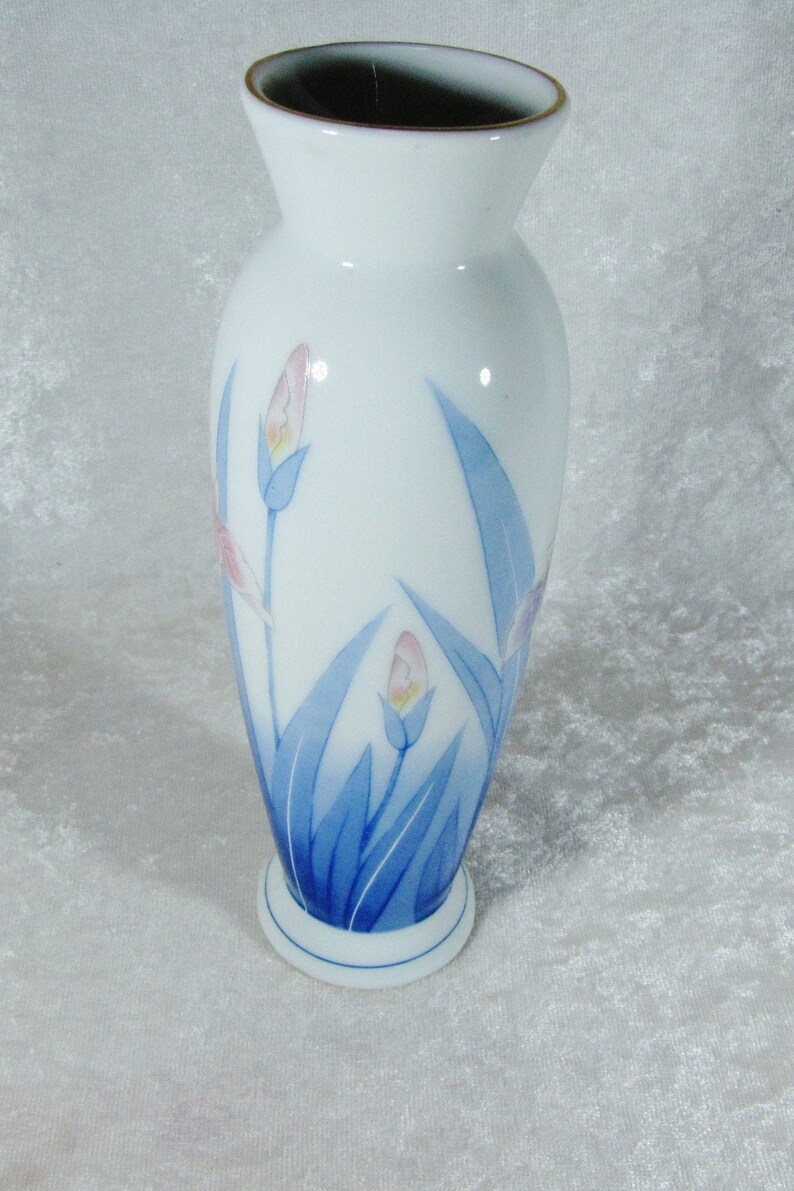 May include: A white ceramic vase with a blue and pink floral design. The vase has a rounded body and a flared top.
