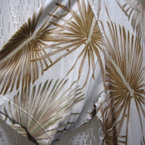 May include: White short-sleeved shirt with a brown and green palm leaf pattern. The shirt's fabric is visible, showing the texture and the stitching of the sleeve.